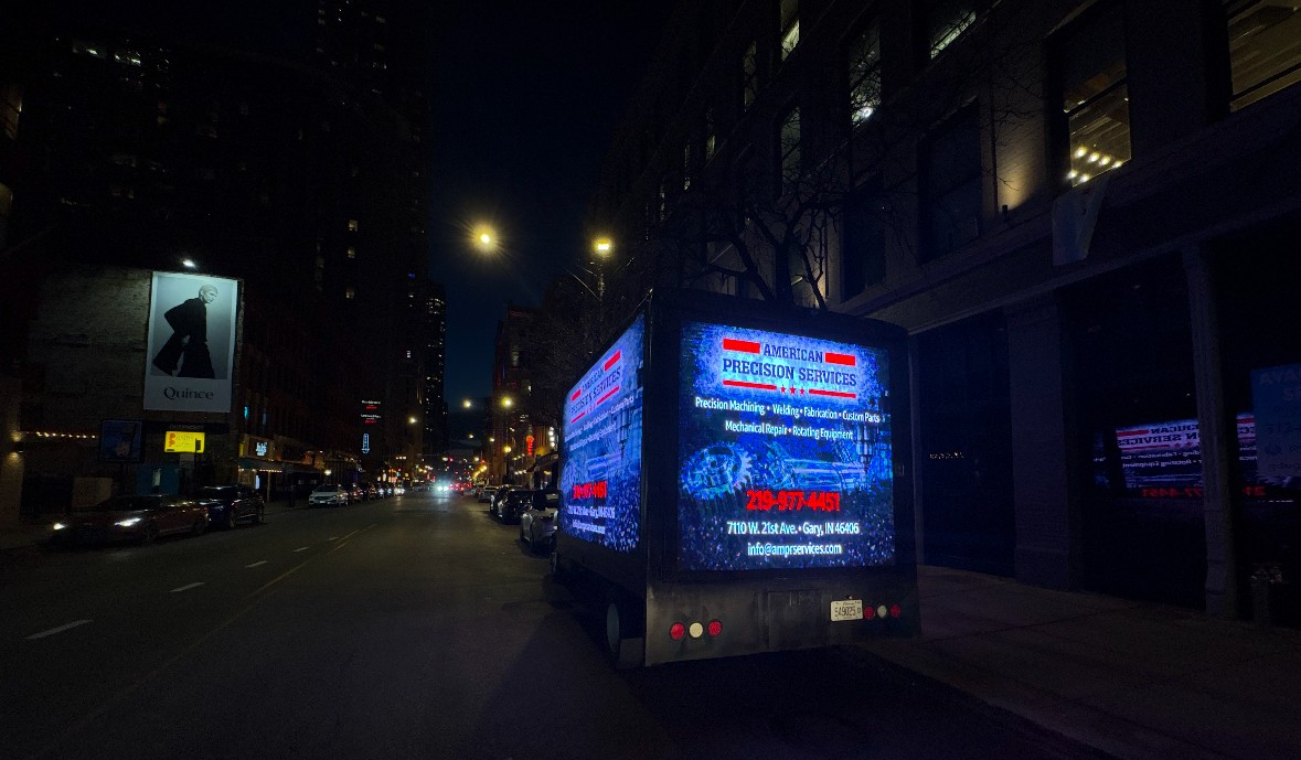AOTC mobile LED truck for American Precision Services glowing on a downtown Chicago street at night