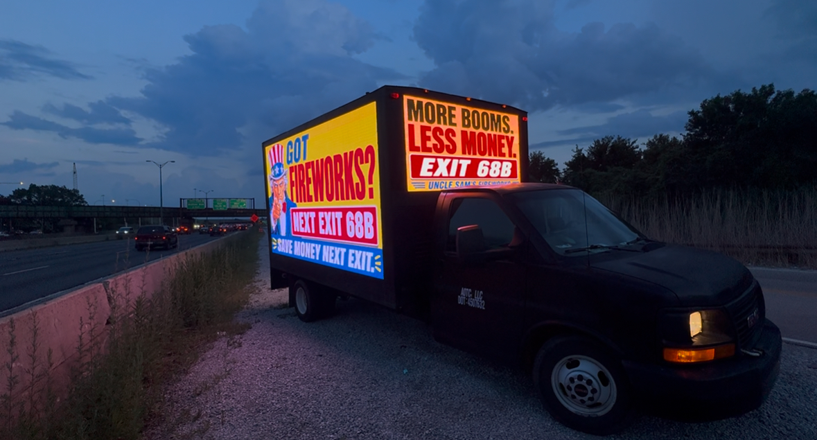 AOTC LED truck for Uncle Sam's Fireworks glowing brightly at dusk beside the highway