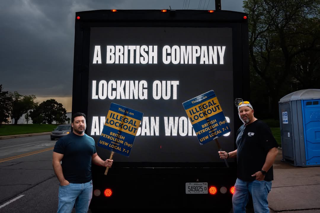Two USW workers holding illegal lockout signs in front of the AOTC LED truck at dusk